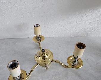 May include: A brass-colored, three-arm ceiling light fixture. Each arm extends from a central base and holds a light socket with a paper sleeve. The fixture is designed for overhead lighting.