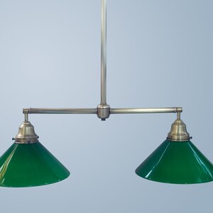 May include: A brass two-light pendant fixture with green glass shades. The fixture has a long, straight rod with two arms extending out to the sides, each holding a green glass shade.