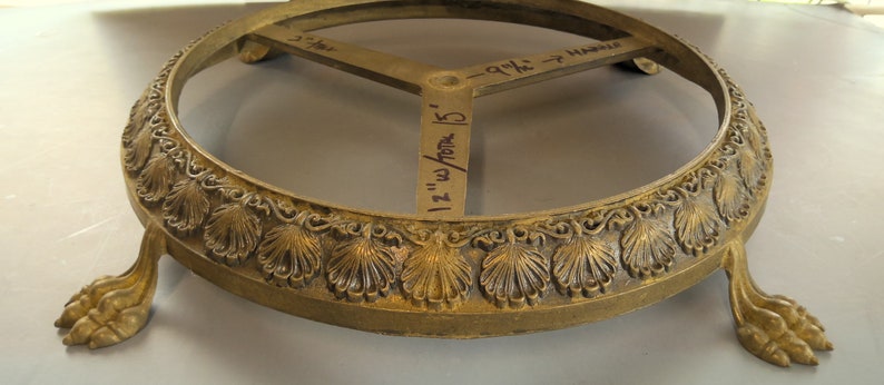 Puede incluir: Base de metal dorado con parte superior redonda y tres patas. La base tiene un dise&ntilde;o decorativo de hojas y un di&aacute;metro de 30,5 cm.