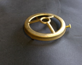 May include: A gold metal lampshade ring with a round shape and a center hole. The ring has three prongs extending from the center hole.