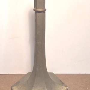 May include: A vintage brass candlestick holder with a geometric design. The base is a wide, multi-sided shape, and the stem is a tall, octagonal column. A small ring encircles the stem. The candlestick holder measures approximately 10 inches tall.