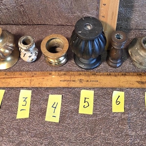 May include: An assortment of eight antique lamp parts, including brass and metal components. A wooden ruler and numbered yellow sticky notes are also present. The parts vary in shape and size, with some showing signs of age and wear.