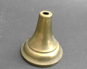 May include: A conical brass-colored metal component with a wide, circular base that tapers upward to a narrow, flat top featuring a small, centered circular opening. The object has a smooth, metallic finish with subtle variations in tone.