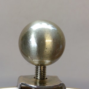 May include: A silver metal ball finial with a threaded stem. The finial is attached to a metal base.