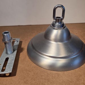 May include: A brushed nickel ceiling canopy kit. The kit includes a round, domed canopy with a loop for hanging, a threaded rod, and a mounting bracket. The components are made of metal and are designed for electrical fixtures.