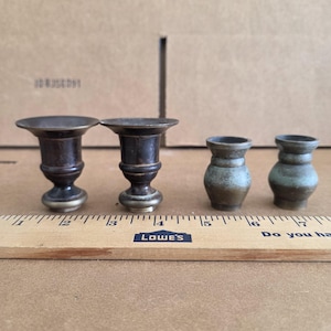 May include: Four small decorative vases. Two are dark brown with a pedestal base and flared top. The other two are smaller, with a green and brown glaze. A wooden ruler with the Lowe's logo is in the foreground.