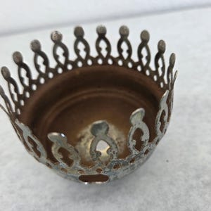 May include: A vintage, silver-toned metal crown-shaped lamp part. The decorative rim features a repeating pattern of stylized arches and small, rounded finials. The interior is a warm, coppery brown.