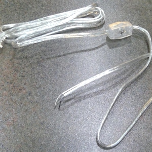 May include: A clear, transparent power cord with a two-prong plug and a small, clear inline switch. The cord is silver and coiled, designed for electrical devices. The plug is a standard US type.