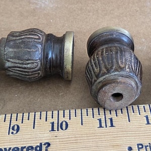 May include: Four decorative wooden finials with a dark brown finish and carved details. Each finial has a brass-coloured ring at the base. A wooden ruler is in the foreground.