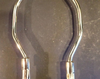 May include: A silver metal lamp harp with a hexagonal base and two curved arms.