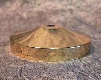 May include: A gold-colored, decorative ceiling canopy with a circular base and a conical top. The canopy has a smooth, reflective surface and a small hole at the top. The item is designed for use with a light fixture.
