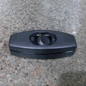 May include: A black, rectangular inline lamp switch with a rounded toggle. The switch has "ON" and "OFF" markings. The switch is on a speckled gray surface.