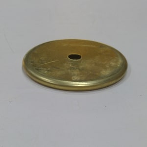 May include: A gold-coloured metal disc with a small hole in the centre. The disc has a slightly raised edge.