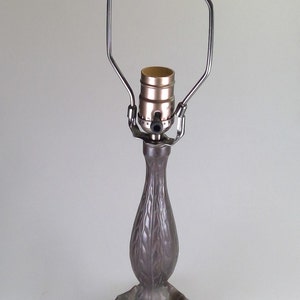 Peut inclure: Une lampe de table en bronze avec une base en forme de feuilles et un abat-jour en métal simple. La lampe a une seule douille et un cordon.