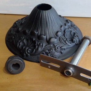 May include: Black metal ceiling light fixture with a decorative floral design. The fixture includes a mounting plate, a threaded rod, and a decorative cap.