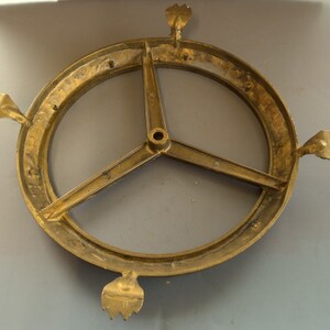 Puede incluir: Una base de metal dorado con tres patas y una parte superior circular. La base tiene un dise&ntilde;o decorativo con un motivo floral.