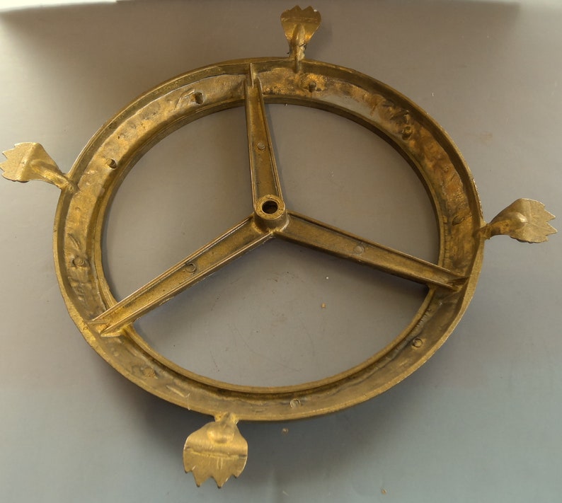 Puede incluir: Una base de metal dorado con tres patas y una parte superior circular. La base tiene un dise&ntilde;o decorativo con un motivo floral.