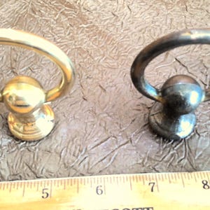 May include: Two metal ring pulls, one gold and one silver, with a round knob on the bottom. The ring pulls are about 1 inch in diameter.