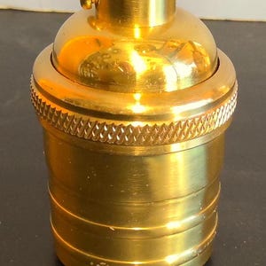 May include: A gold-colored metal light bulb socket with a threaded top and a textured base.