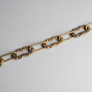 May include: A close-up of a brass chain with ornate links. The chain is broken, with one link separated from the rest.