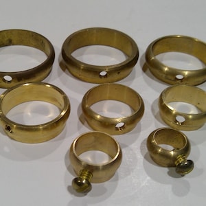May include: A collection of brass rings of varying sizes, each with a small hole. One ring has a screw. The rings are a warm gold color and appear to be vintage or antique hardware.