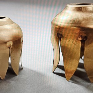 May include: Two gold metal candle holders with a scalloped design. The larger holder is in the background and the smaller holder is in the foreground.