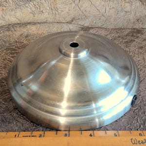 May include: A silver metal lampshade with a round top and a hole in the centre. The shade is approximately 15 cm in diameter.
