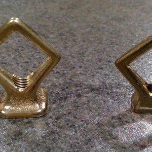May include: Two gold-colored metal diamond-shaped hooks with threaded bases.