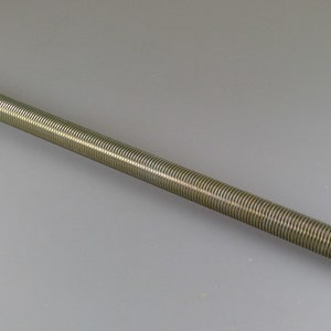 May include: A threaded rod with a metallic finish. The rod is cylindrical and covered in fine, evenly spaced threads. The rod is angled across a gray surface.
