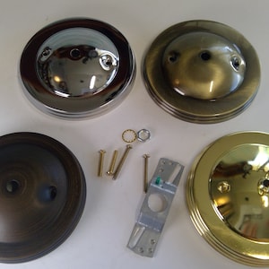 May include: Four ceiling light fixture canopy plates in different finishes: polished chrome, antique brass, oil rubbed bronze, and polished brass. The plates are round and have three holes for mounting. The set also includes mounting screws and a metal mounting bracket.
