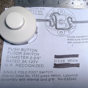 May include: White push button floor switch with a 2-2/5 inch diameter. The switch is rated for 3 amps and 125 volts. It is a single pole foot switch with an internal cord grip. The text "D338 White" is written on the switch.