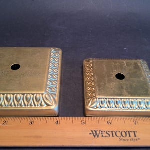 May include: Two gold metal lamp bases with a decorative border and a hole in the center. The larger base is 4 inches wide and the smaller base is 3 inches wide.