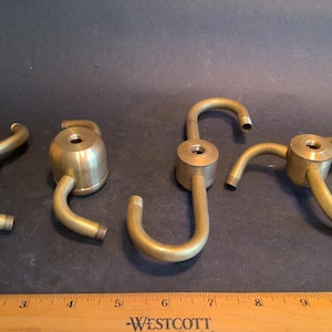 May include: Five brass ceiling light fixture canopy adapters with three prongs each. The adapters are designed to connect to a ceiling fixture and have a threaded opening for a light bulb.