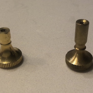 May include: Two brass lamp finials with a fluted base and a threaded top. The finials are different sizes.