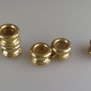 May include: Four gold-colored metal beads, three of which are stacked on top of each other. The beads are round and have a smooth, shiny finish.