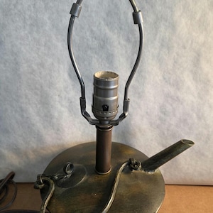 May include: Vintage table lamp with a bronze finish. The lamp has a round base with a spout and a decorative handle. The lamp has a metal shade holder and a brass finial. The lamp is supported by a paw-shaped foot.