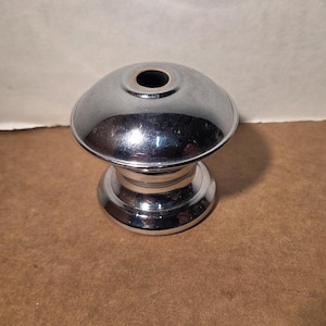 May include: A polished chrome metal object with a rounded, dome-shaped top featuring a central circular opening. The base is wider and circular, connecting to the upper dome section with a smooth, reflective finish throughout the entire piece.