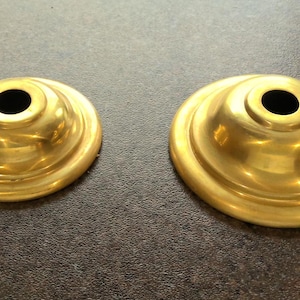May include: Two gold-colored metal lamp finials with a round, slightly domed top and a center hole. The finials have a smooth, shiny finish.