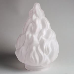 Puede incluir: Objeto decorativo de vidrio blanco esmerilado con un diseño en forma de llama. El objeto tiene una base redondeada y una forma texturizada y fluida, que se asemeja a una llama estilizada. La forma general es suave y elegante.