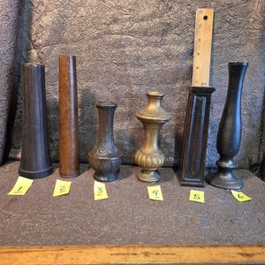 May include: A collection of six decorative objects, likely finials or vase components, in various shapes and materials. The objects are numbered with yellow sticky notes. A wooden ruler is also present.