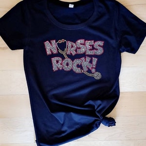 May include: A navy blue t-shirt with the text "NURSES ROCK!" in rhinestones. The text includes a red heart and a stethoscope.