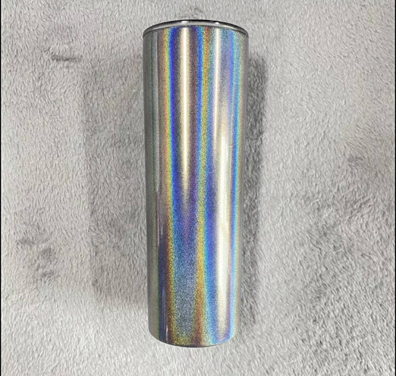 May include: A silver tumbler with a holographic finish. The tumbler has a smooth, shiny surface with a rainbow effect.
