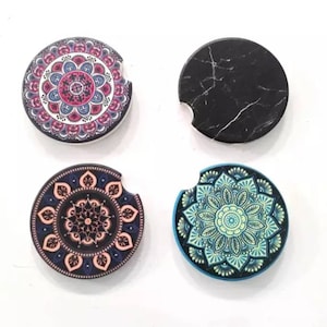 May include: Four round coasters with different designs. One coaster features a black and white marble pattern. The other three coasters feature colorful mandala designs with pink, orange, and blue accents.