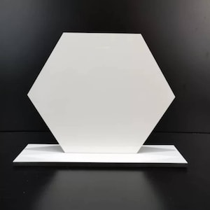 May include: A white hexagonal display stand with a flat surface. The stand is made of a smooth, glossy material and has a simple, modern design.