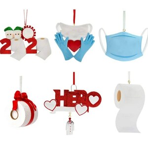 May include: Set of six Christmas ornaments with a 2020 theme. The ornaments feature a toilet paper roll, a face mask, a heart with a face mask, a toilet paper roll with a red bow, a toilet paper roll with the word "HERO" and a doctor's coat.
