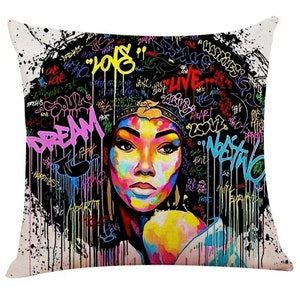May include: Square throw pillow with a vibrant graffiti art design. The pillow features a colorful portrait of a woman with an afro, adorned with a crown. The background is filled with graffiti text in various colors, including pink, yellow, and blue.