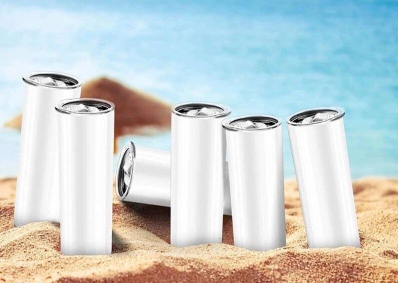 Puede incluir: Seis vasos de acero inoxidable blanco con tapas plateadas, dispuestos sobre un fondo de playa de arena.