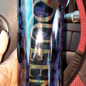 May include: A black and blue tumbler with a gold glitter design and the word "QUEEN" written in gold glitter. The tumbler has a straw and a lid.