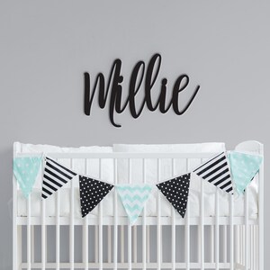 May include: A white crib with a black and white patterned bunting hanging above it. The name "Millie" is written in black script on the wall above the crib.