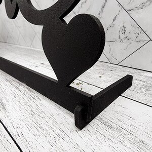 May include: Black metal sign with the word "Love" in a stylized font. The sign has a heart shape at the top and a flat base.